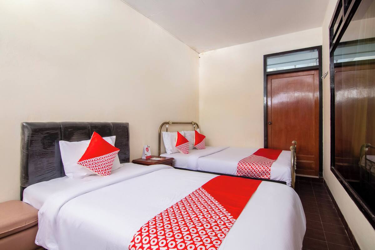 A hotel room with two beds, each with a patterned bedspread and pillows, a wooden door, and a window with a view.