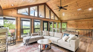 A spacious living room with a large sectional sofa, a round coffee table, and a view of the outdoors through large windows. - Perfect Family Retreat MTN Views Pool Privacy (Sevierville)
