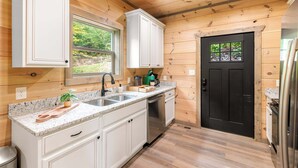 A compact kitchen with white cabinets, a granite countertop, a black door, and a stainless steel refrigerator. - Perfect Family Retreat MTN Views Pool Privacy (Sevierville)