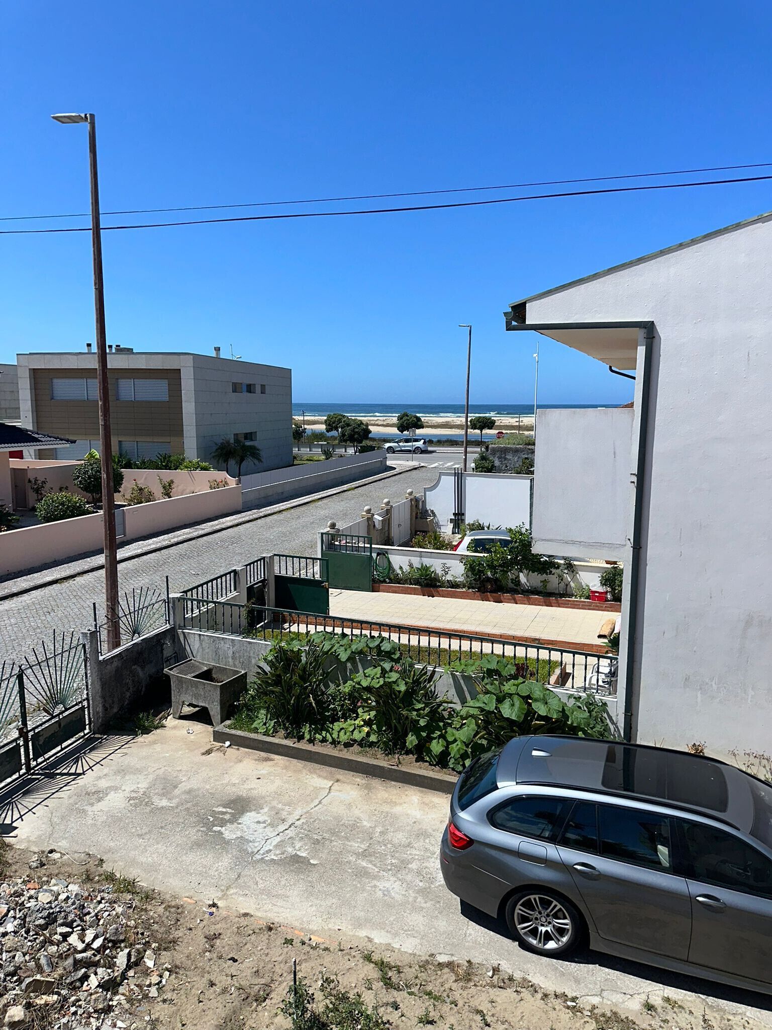 Zona residencial con vista al mar, un coche estacionado en la calle y un edificio de fachada blanca.