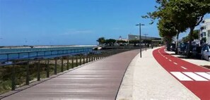 Une promenade en bord de mer avec un chemin rouge, bordée d’une route où sont garées des voitures, et sous un ciel bleu dégagé.