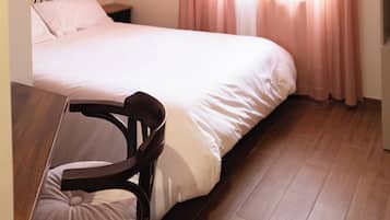 Un dormitorio con cama, una silla, una mesita de noche y una ventana con cortinas.