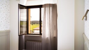 Un dormitorio con ventana, radiador y vistas a un paisaje verde.