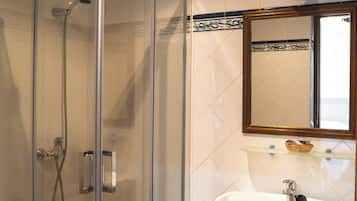 A bathroom with a glass-enclosed shower, a white sink with a mirror above it, and a shelf with toiletries.