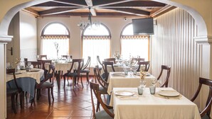 Un comedor con varias mesas y sillas, techos abovedados y ventanas amplias con cortinas.