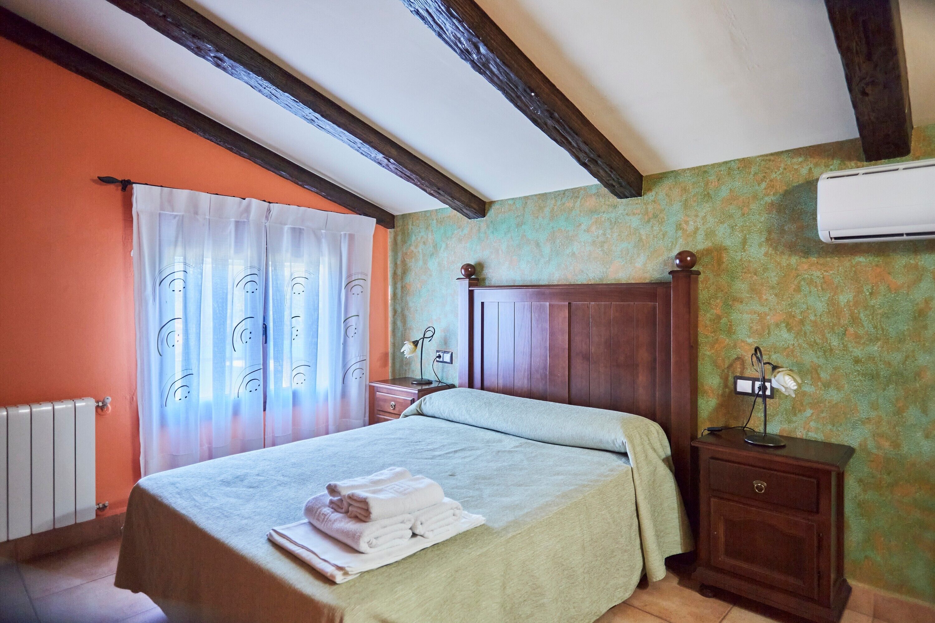 Un dormitorio con cama, mesita de noche, cabecera de madera, radiador y aire acondicionado.