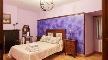 Un dormitorio con cama, mesitas de noche, cómoda, candelabro, chimenea y una pared con diseño texturizado morado.