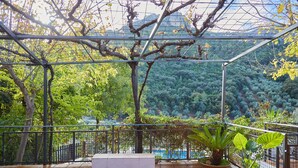 A covered balcony with a view of a forested area, a white bench, and potted plants. - Rural House 'Fuente Los Avellanos' with Mountain View, Wi-Fi and Air Conditioning (Villanueva del Arzobispo)
