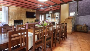 A dining area with wooden chairs and a table, a fireplace, a kitchen with cabinets and a microwave, and a staircase leading to an upper level. - Rural House 'Fuente Los Avellanos' with Mountain View, Wi-Fi and Air Conditioning (Villanueva del Arzobispo)