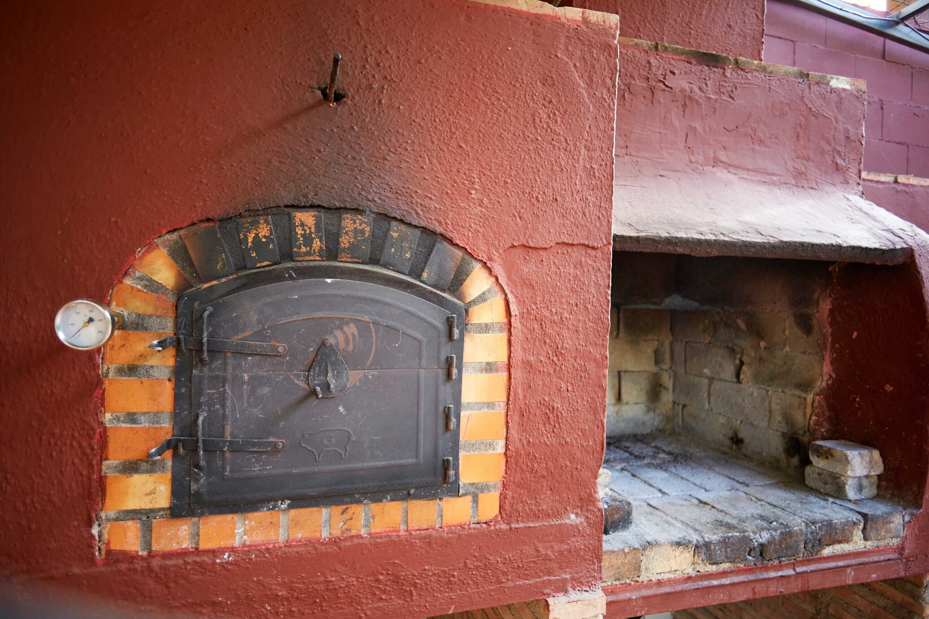 A brick oven with a metal door, a thermometer, and a brick base.