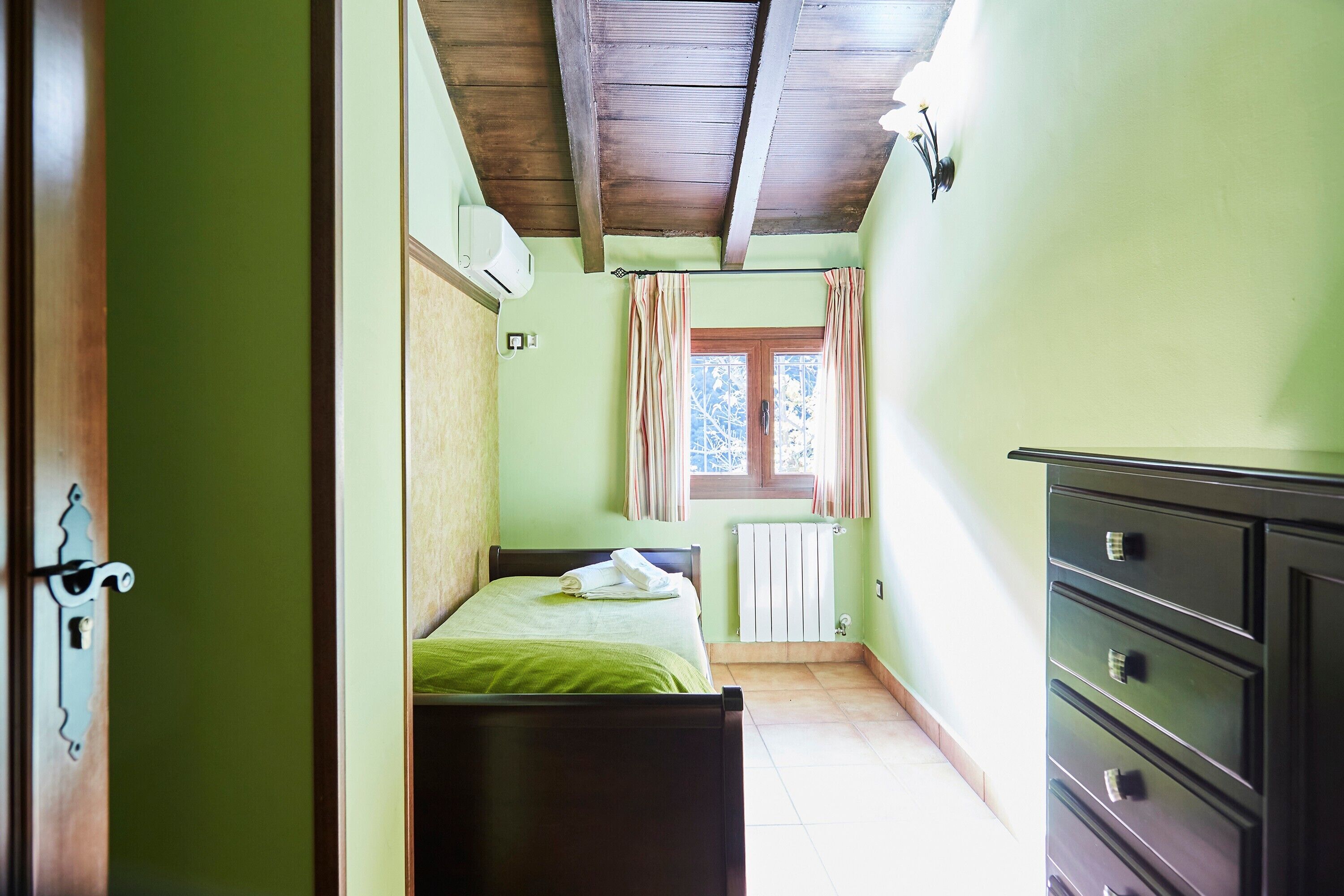Une chambre à coucher avec un lit, une commode, un radiateur et une fenêtre avec des rideaux.