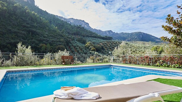 A swimming pool with a view of mountains, a lounge chair, and a small wooden structure. - Rural House 'Fuente Los Avellanos' with Mountain View, Wi-Fi and Air Conditioning (Villanueva del Arzobispo)