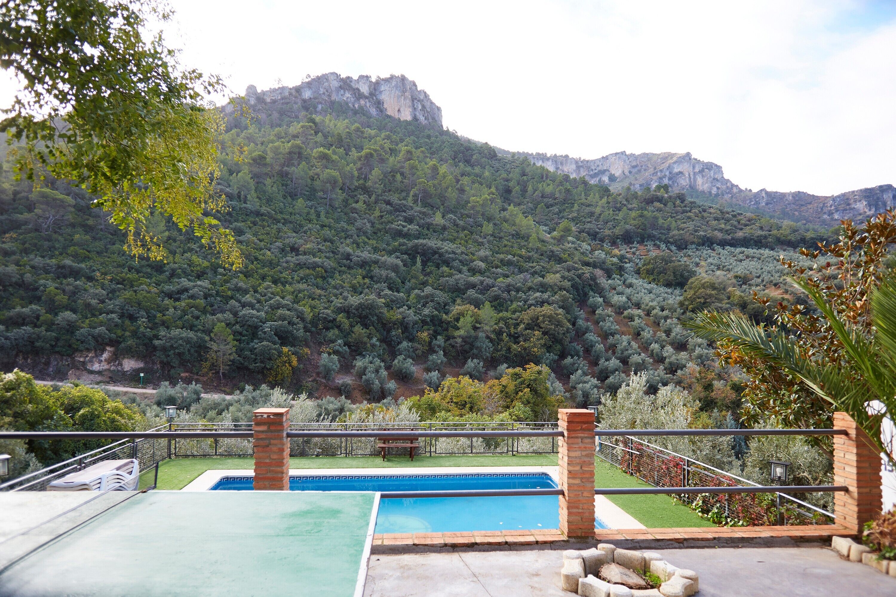 Una piscina con montañas al fondo, un área de patio y vistas a una ladera boscosa.