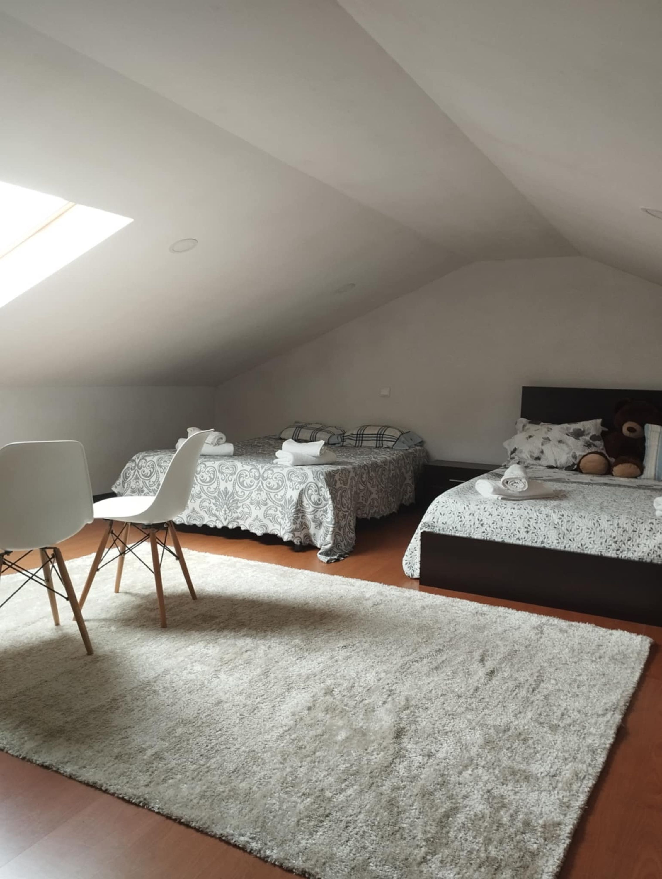 A bedroom with two beds, a white chair, and a large window.