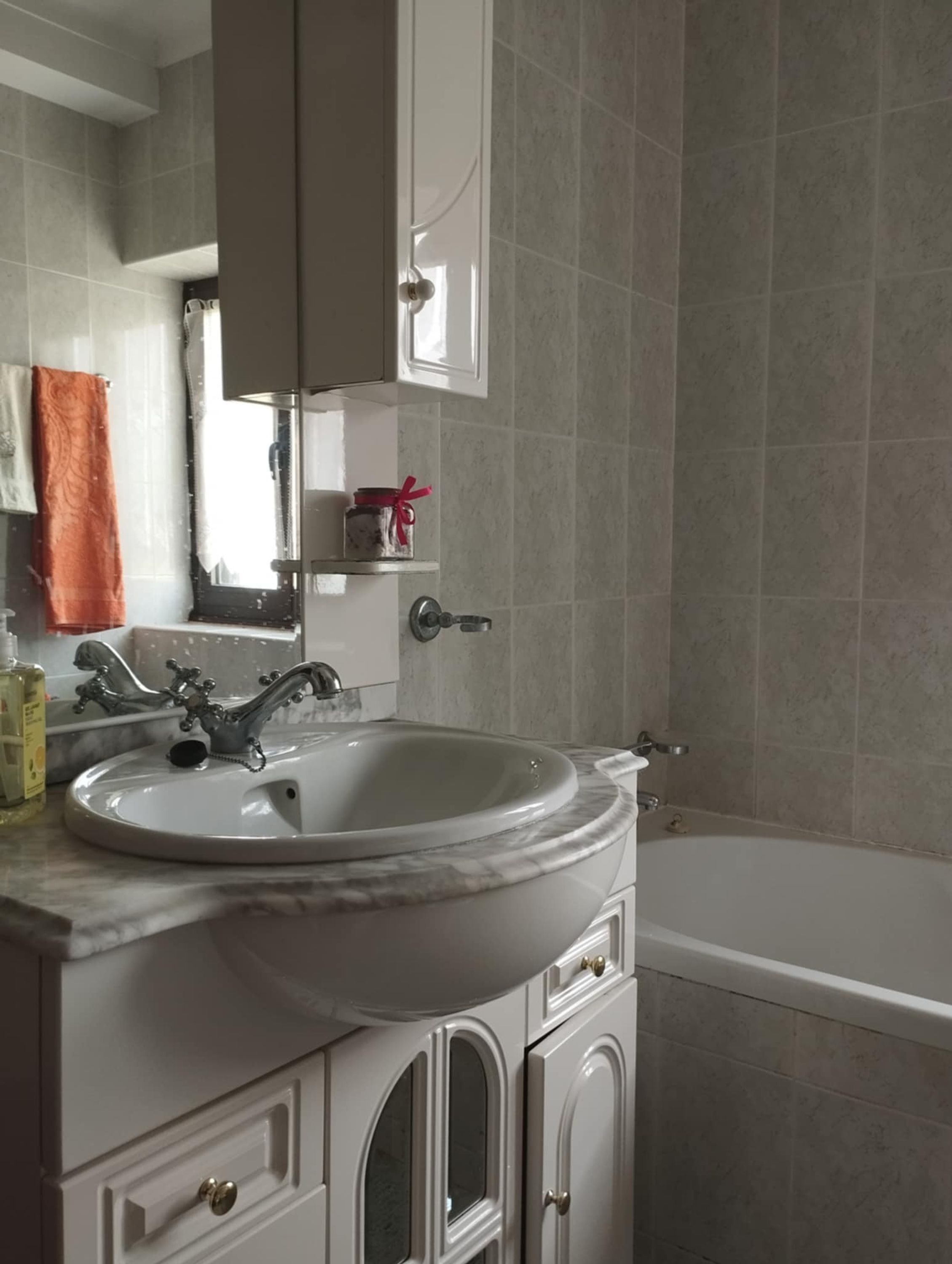 Une salle de bain avec un lavabo blanc, un miroir, un meuble et une baignoire.
