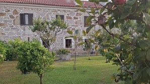 Un bâtiment en pierre avec un toit en tuiles, entouré d’une pelouse bien entretenue et de diverses plantes en pot.