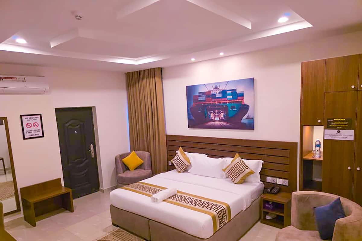 A hotel room with a large bed, a chair, a desk, and a painting on the wall.