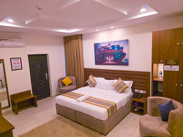 A hotel room with a large bed, a chair, a desk, and a painting on the wall.
