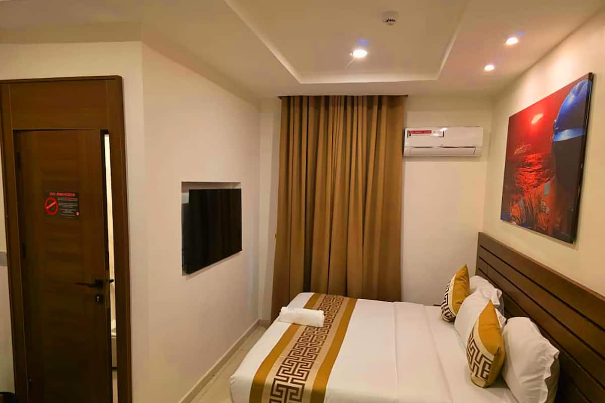 A hotel room with a bed, a television, an air conditioning unit, and a door with a no smoking sign.