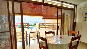 Un coin repas avec une table et des chaises, une vue sur une piscine et une porte-fenêtre coulissante.