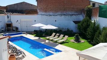 Une piscine entourée d’un mur de briques et d’une pelouse, avec des chaises longues et des parasols à proximité.