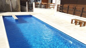Une piscine rectangulaire à l’eau d’un bleu limpide, entourée d’une terrasse carrelée et de bancs en bois.