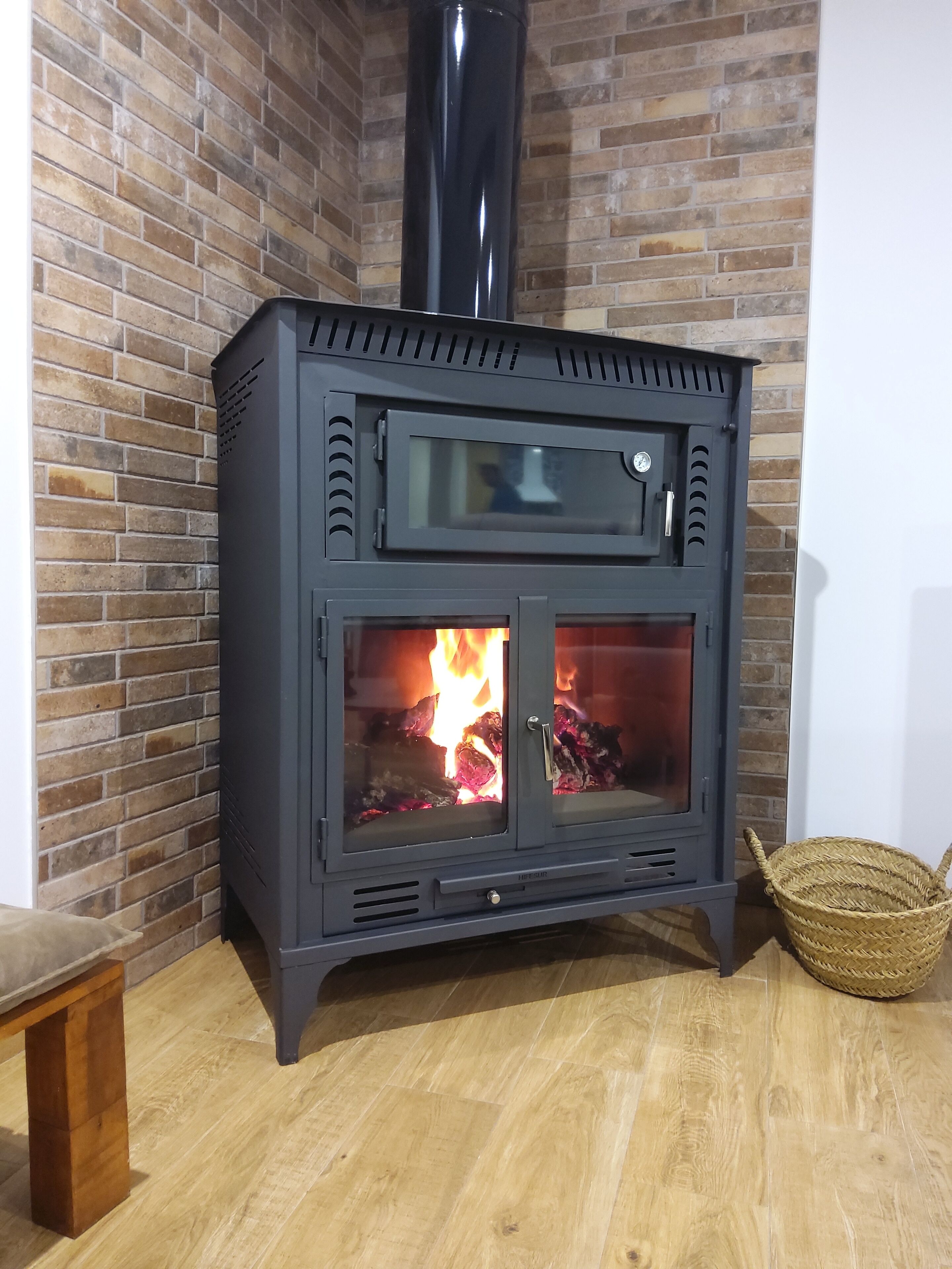 A wood-burning stove with a glass door, set against a brick wall.