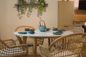 Une table de salle à manger ronde, entourée de chaises en osier, et agrémentée d’un service à thé en céramique de couleur turquoise.
