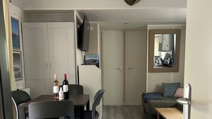 A dining area with a table and chairs, a television mounted above the table, and a sofa in the background. - Voyage Home Mobile Home. Modern facilities on a 4-star campsite (Gassin)