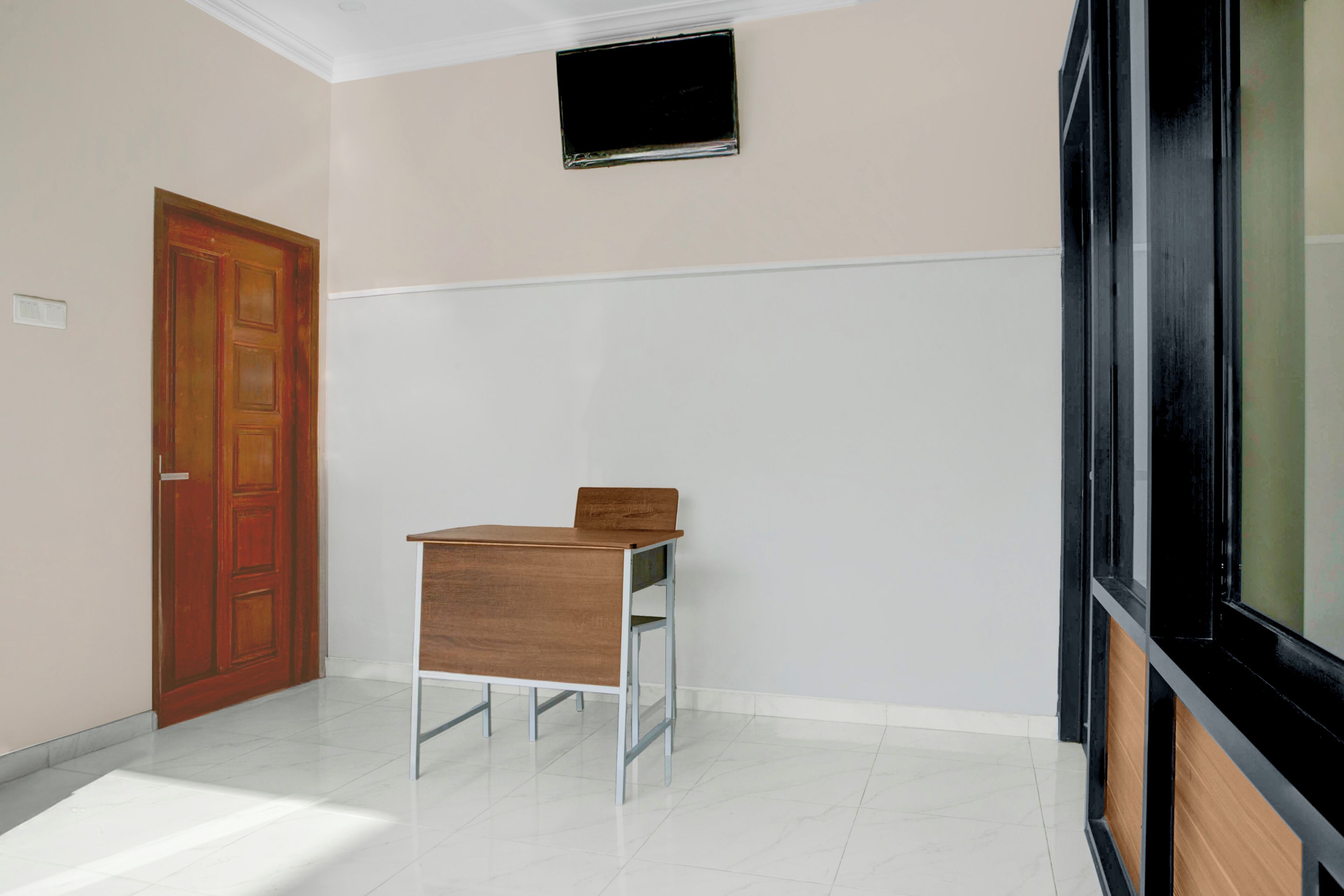 A room with a wooden door, a small table, a white wall, and a window with a black frame.