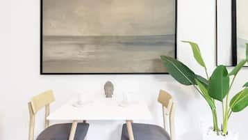A dining area with a white table, two chairs, a Buddha statue, and a large abstract painting on the wall.