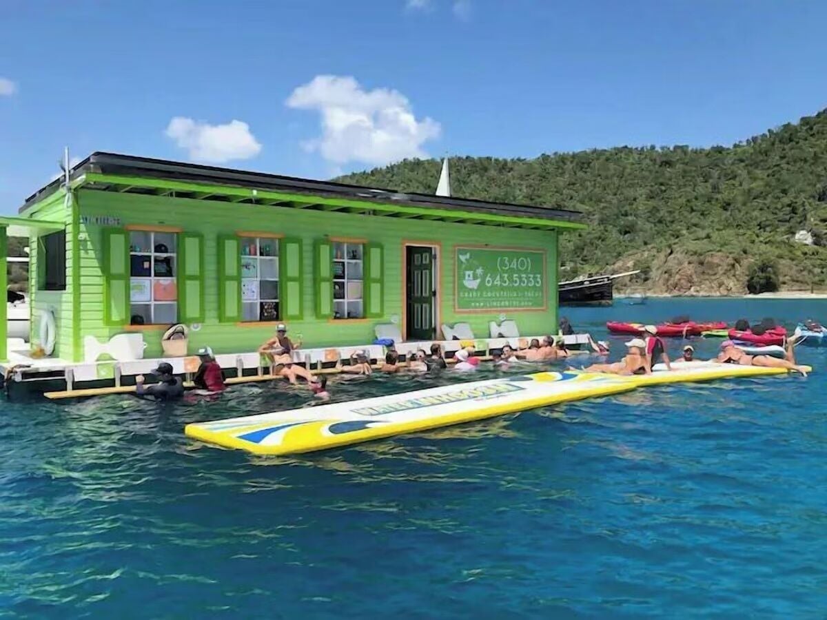 A green building with a pool area, a lifeguard tower, and a beachside view.