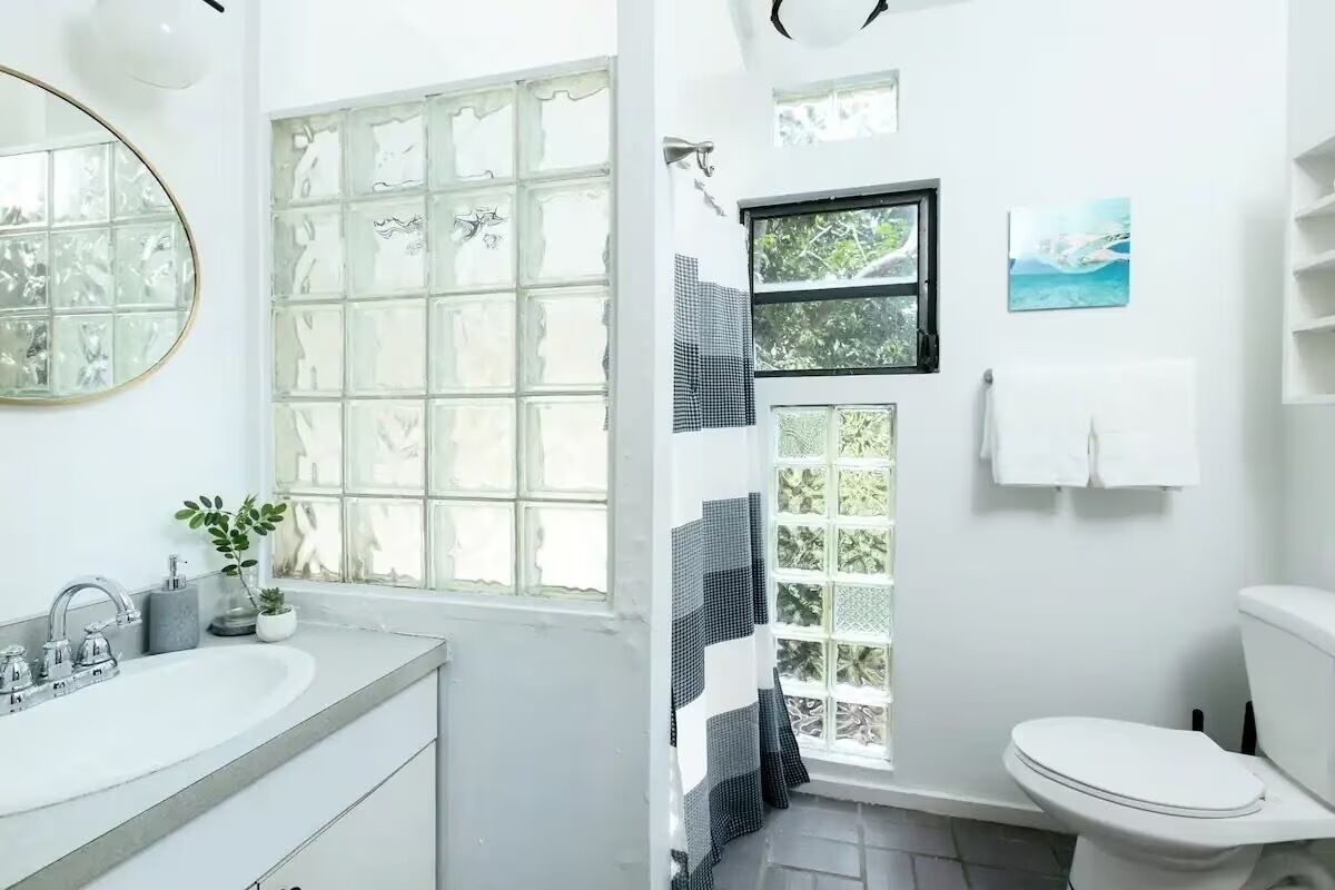 Un baño con un ventanal grande, un lavabo, un inodoro y un espejo.