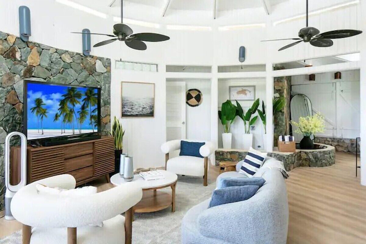 A spacious living room with a stone wall, a large flat-screen TV, and ceiling fans.