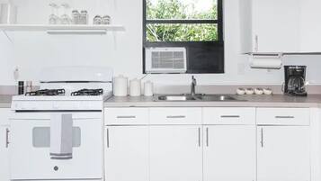 A kitchen with white cabinets, a stove, a sink, and a window with a view of greenery.