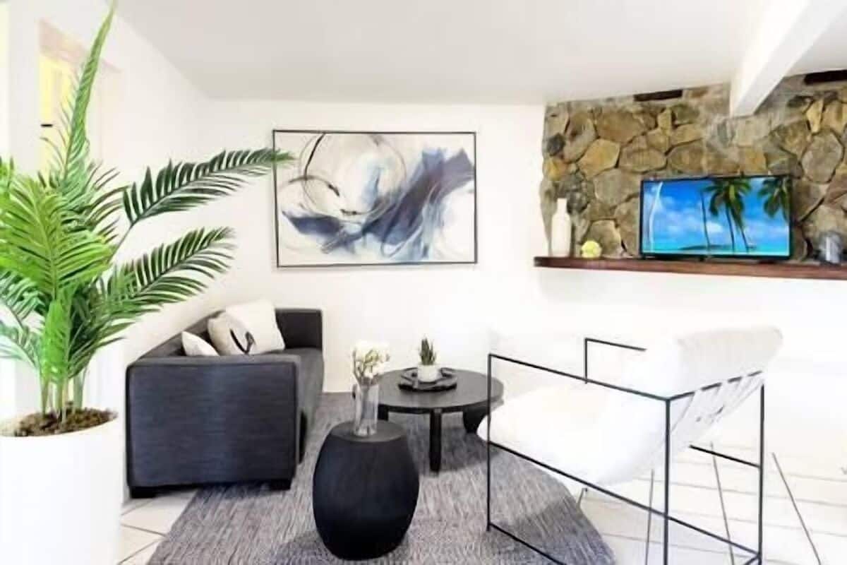 A modern living room with a grey sofa, a black coffee table, a white chair, a large abstract painting, a potted plant, and a stone wall with a TV.
