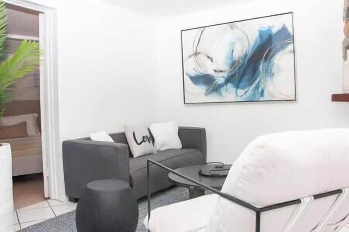 Una sala de estar moderna con un sofá gris, un sillón blanco, una mesa de centro y un cuadro en la pared.