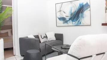 Una sala de estar moderna con un sofá gris, un sillón blanco, una mesa de centro y un cuadro en la pared.