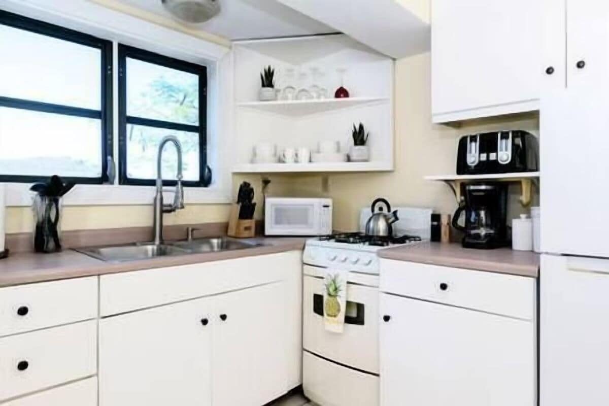 Una cucina compatta con mobili bianchi, un forno a microonde, un bollitore e una macchina per il caffè.