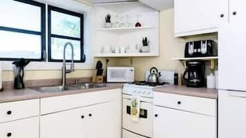 Una cucina compatta con mobili bianchi, un forno a microonde, un bollitore e una macchina per il caffè.