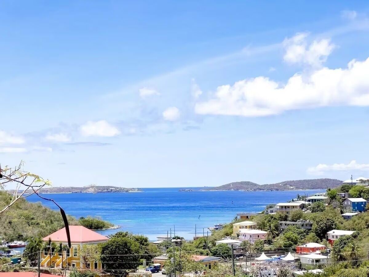 Una località costiera con edifici vicino al mare, cielo sereno e colline in lontananza.