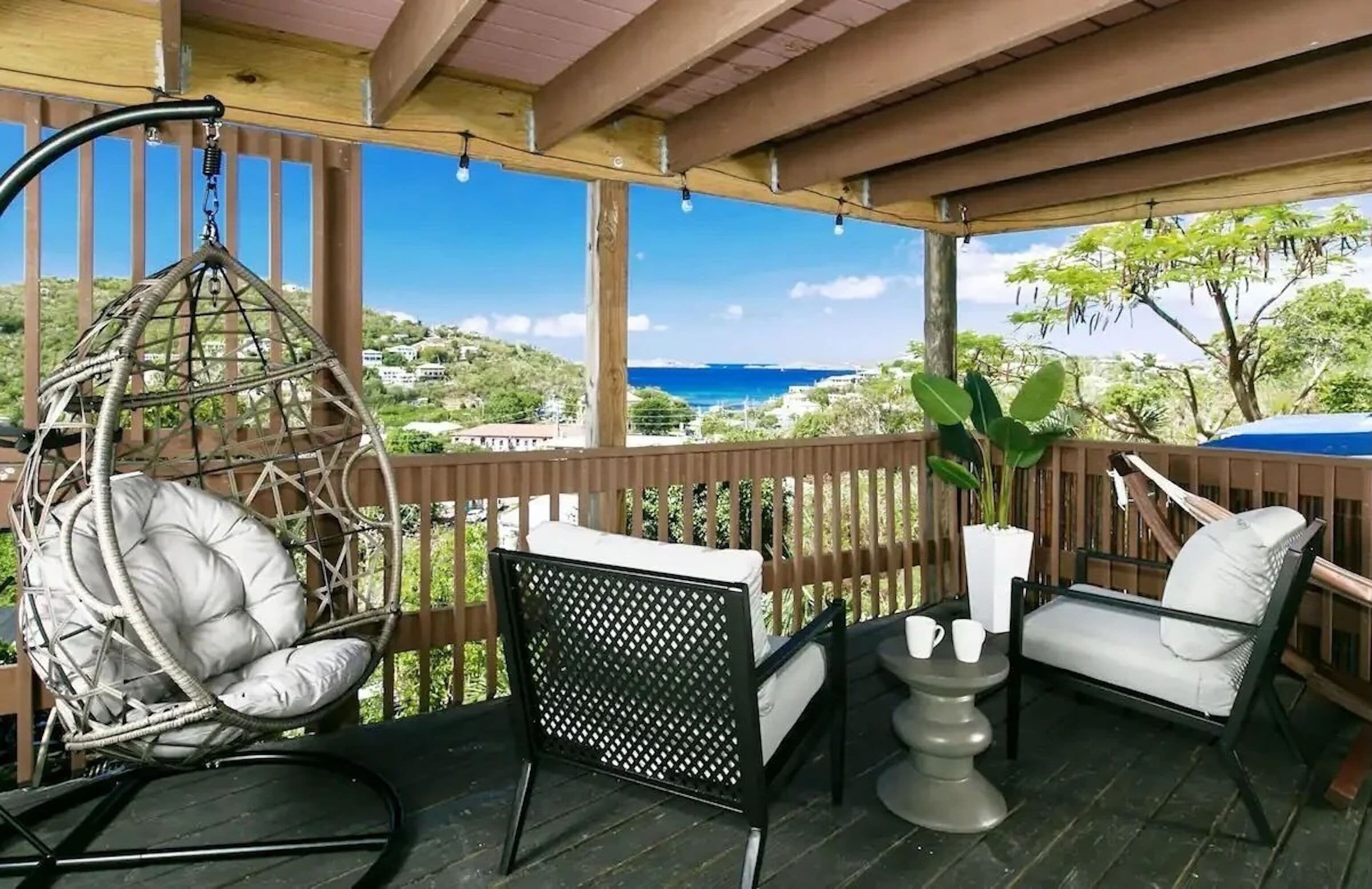 A covered outdoor seating area with wicker chairs and a hanging chair, overlooking a scenic view.