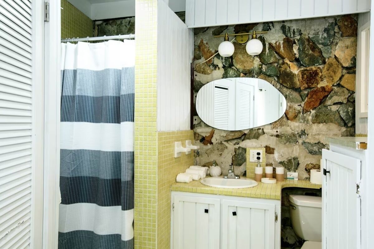 A bathroom with a stone wall, a white sink, and a mirror.