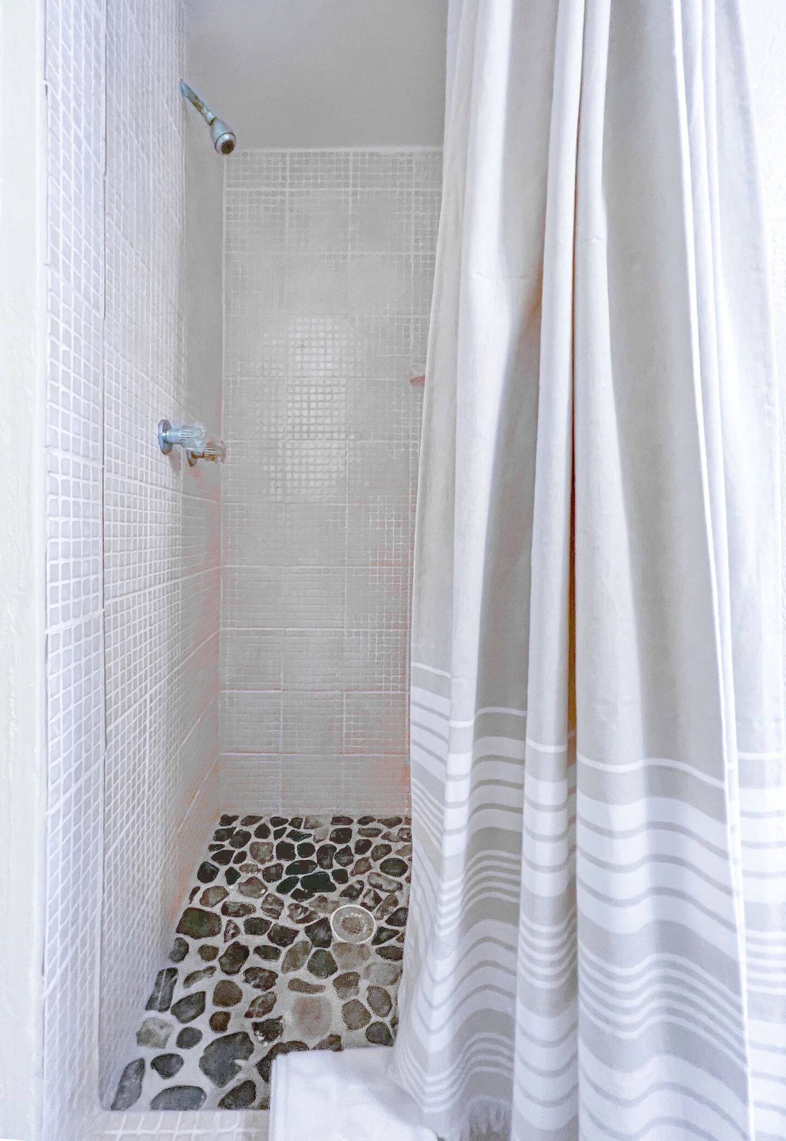 A shower with a tiled wall and a shower curtain.
