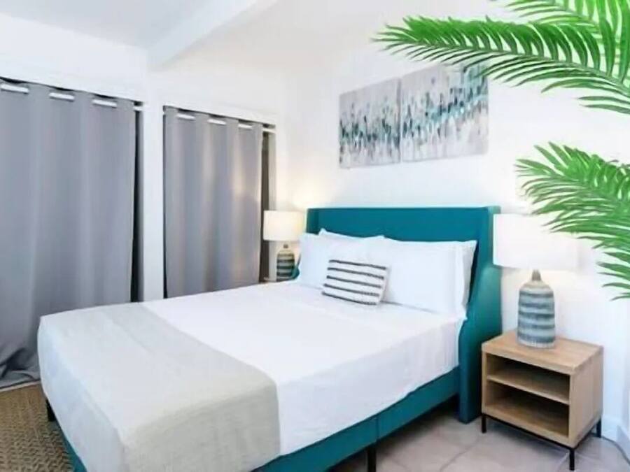 A hotel room with a bed, curtains, a nightstand, a lamp, and a wall art piece.