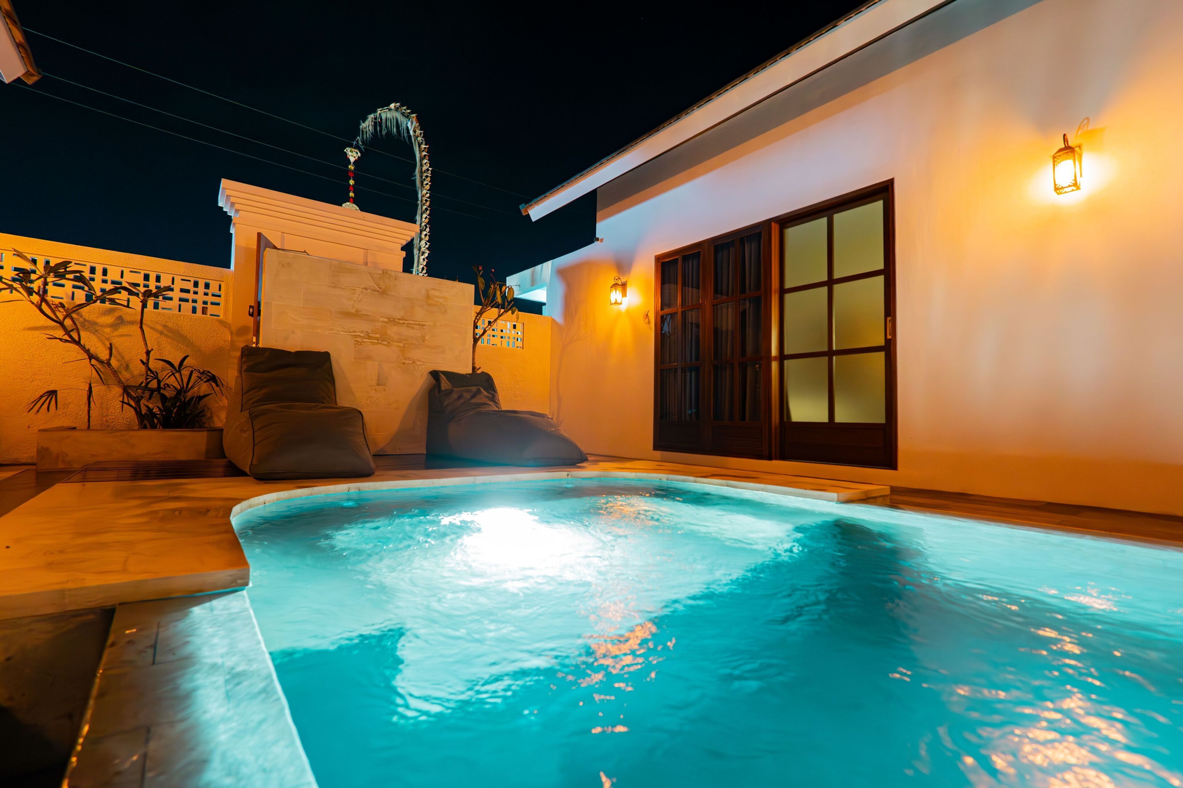 A swimming pool with a tiled deck, a small waterfall feature, and a seating area with cushions.