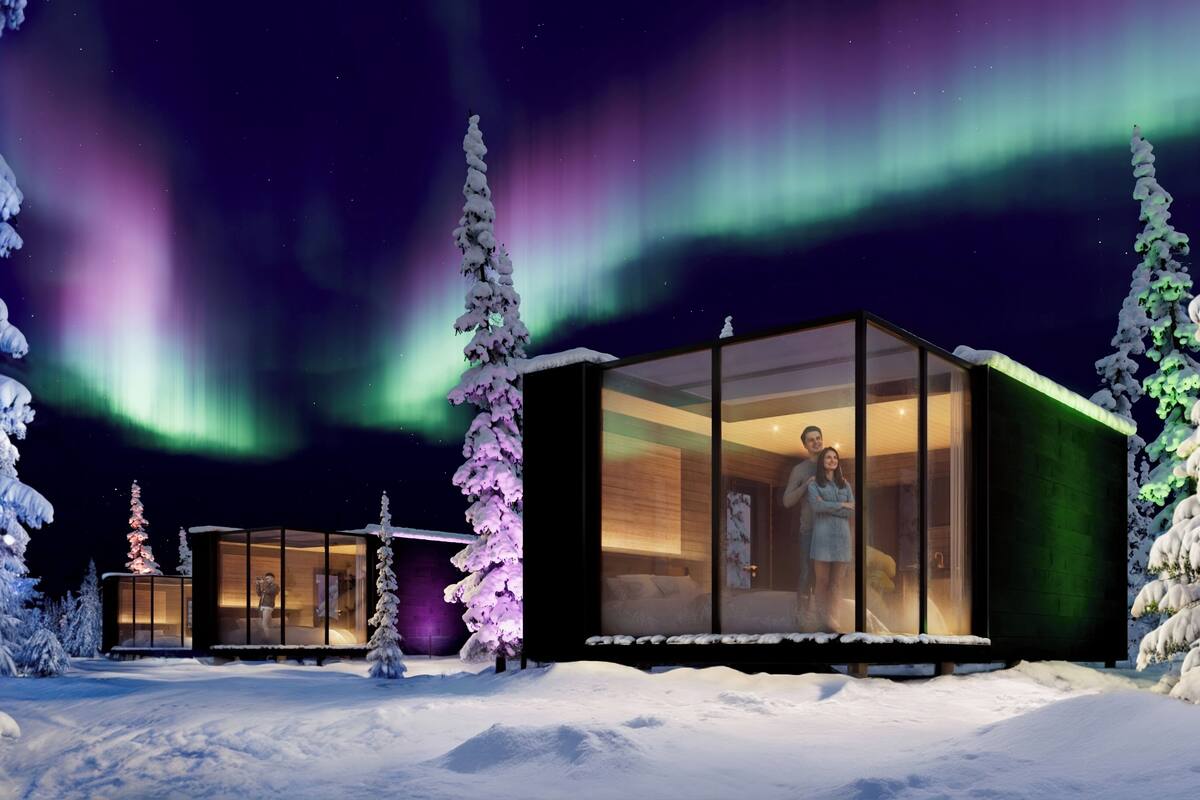 Un edificio moderno de vidrio con una persona en su interior, rodeado de árboles cubiertos de nieve y las auroras boreales.