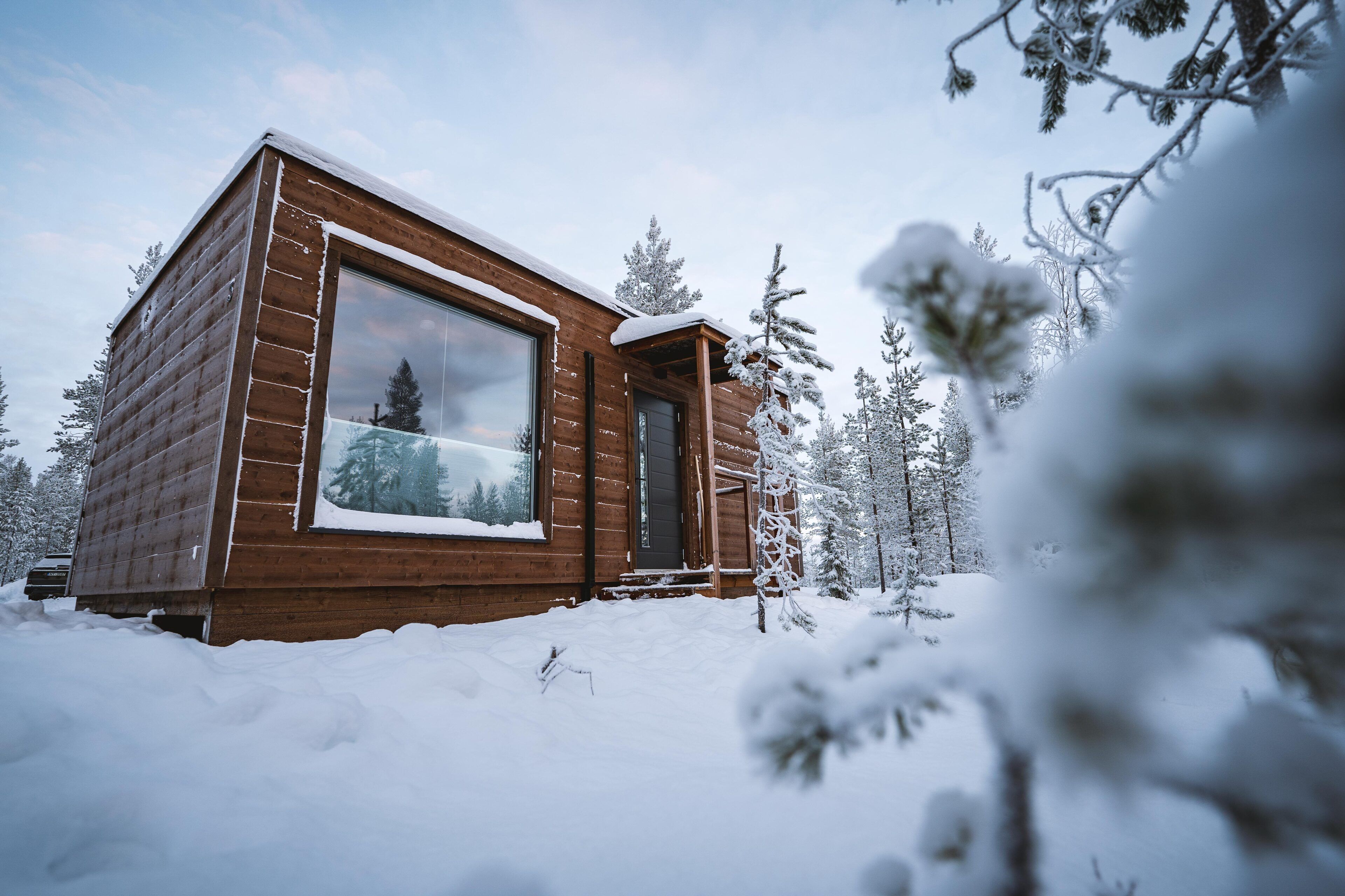 A wooden cabin with a large window, surrounded by snow-covered trees.
