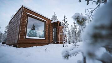 A wooden cabin with a large window, surrounded by snow-covered trees.