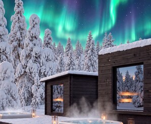 A wooden cabin with a hot tub and a window overlooking a snowy forest under the aurora borealis.